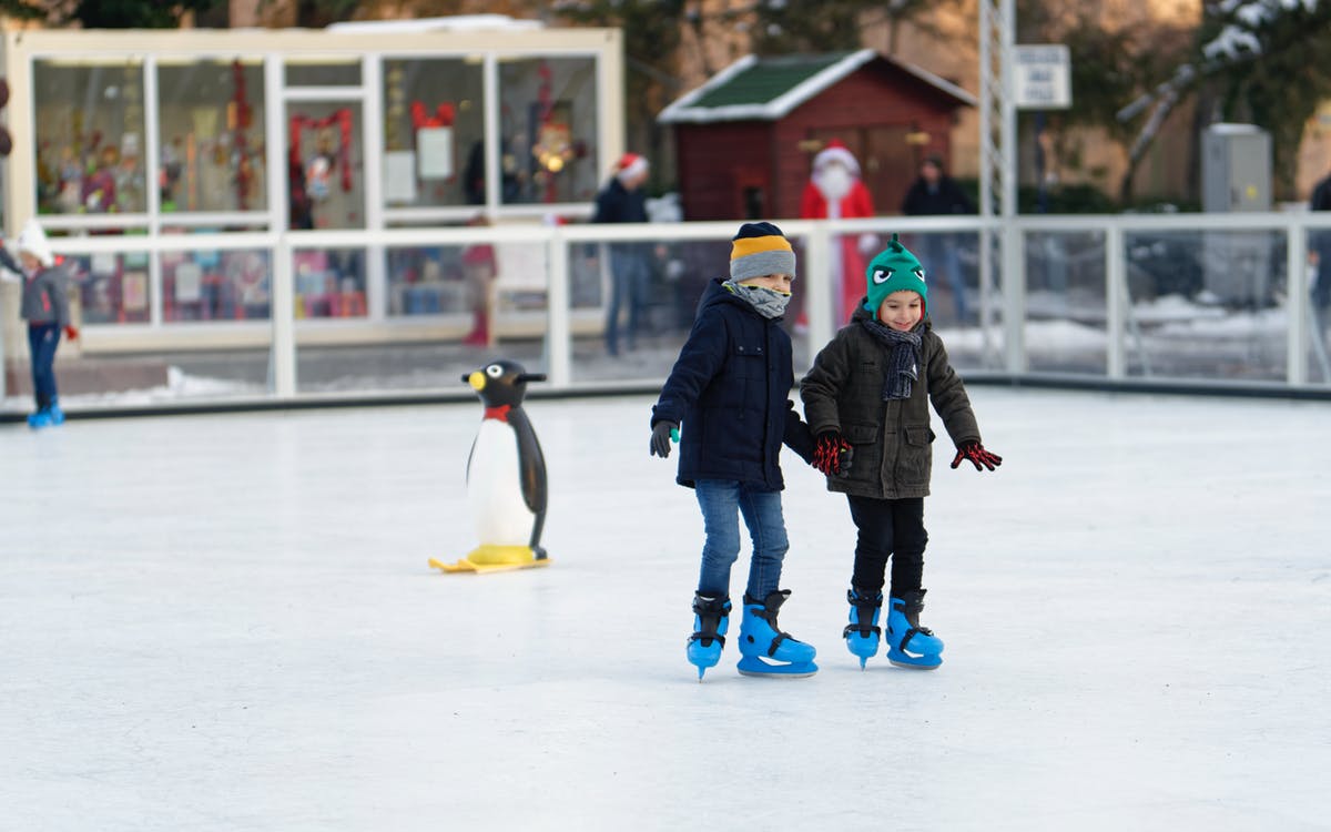Two young children ice skating with a penguin skate aid